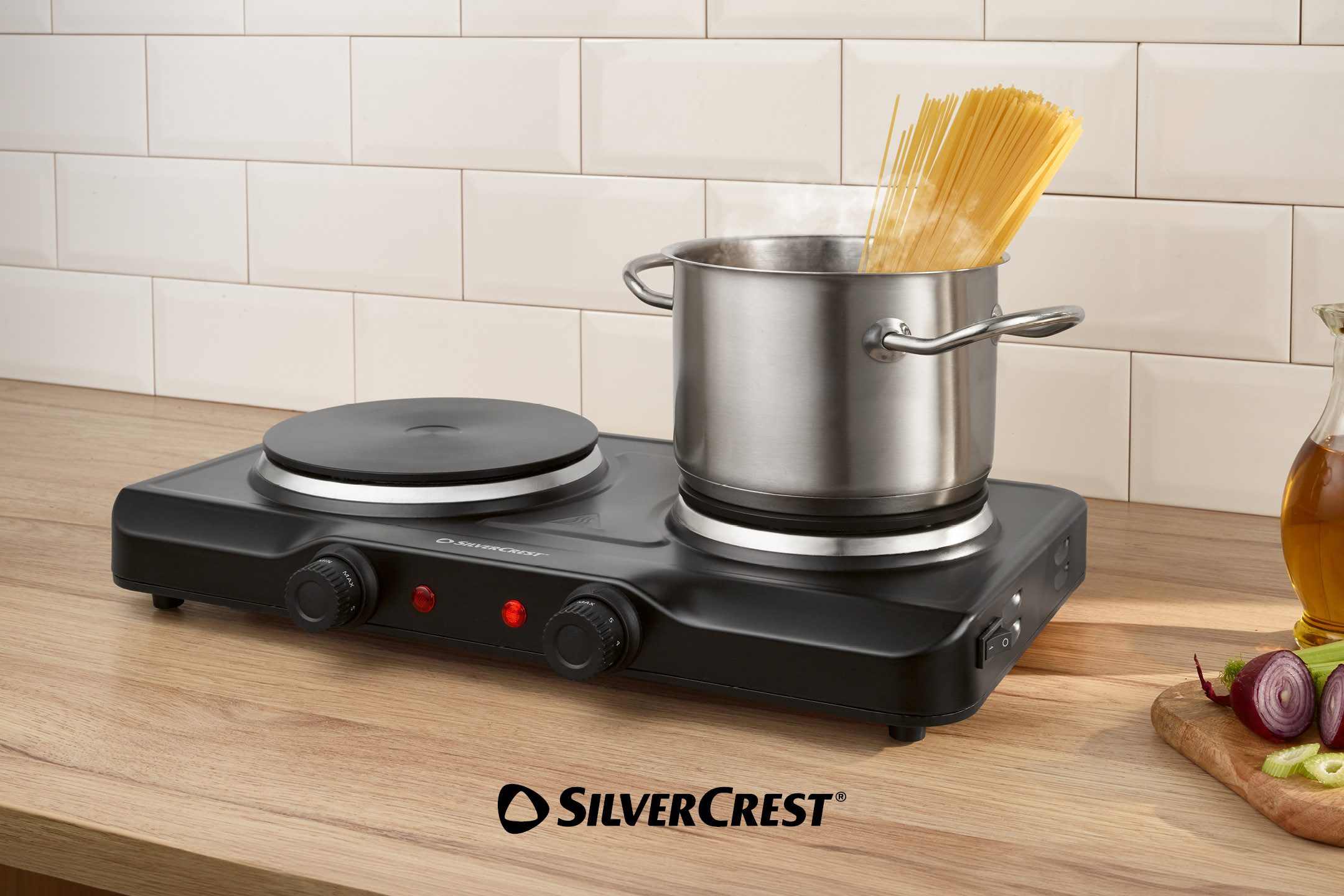 Black double hot plate with a pot of boiling spaghetti, on a wooden kitchen counter.
