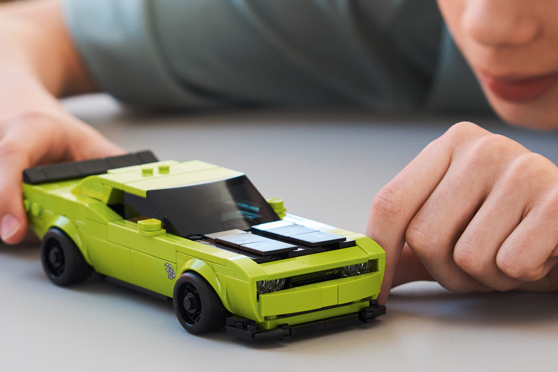 Child playing with a bright green toy car on a light grey surface.