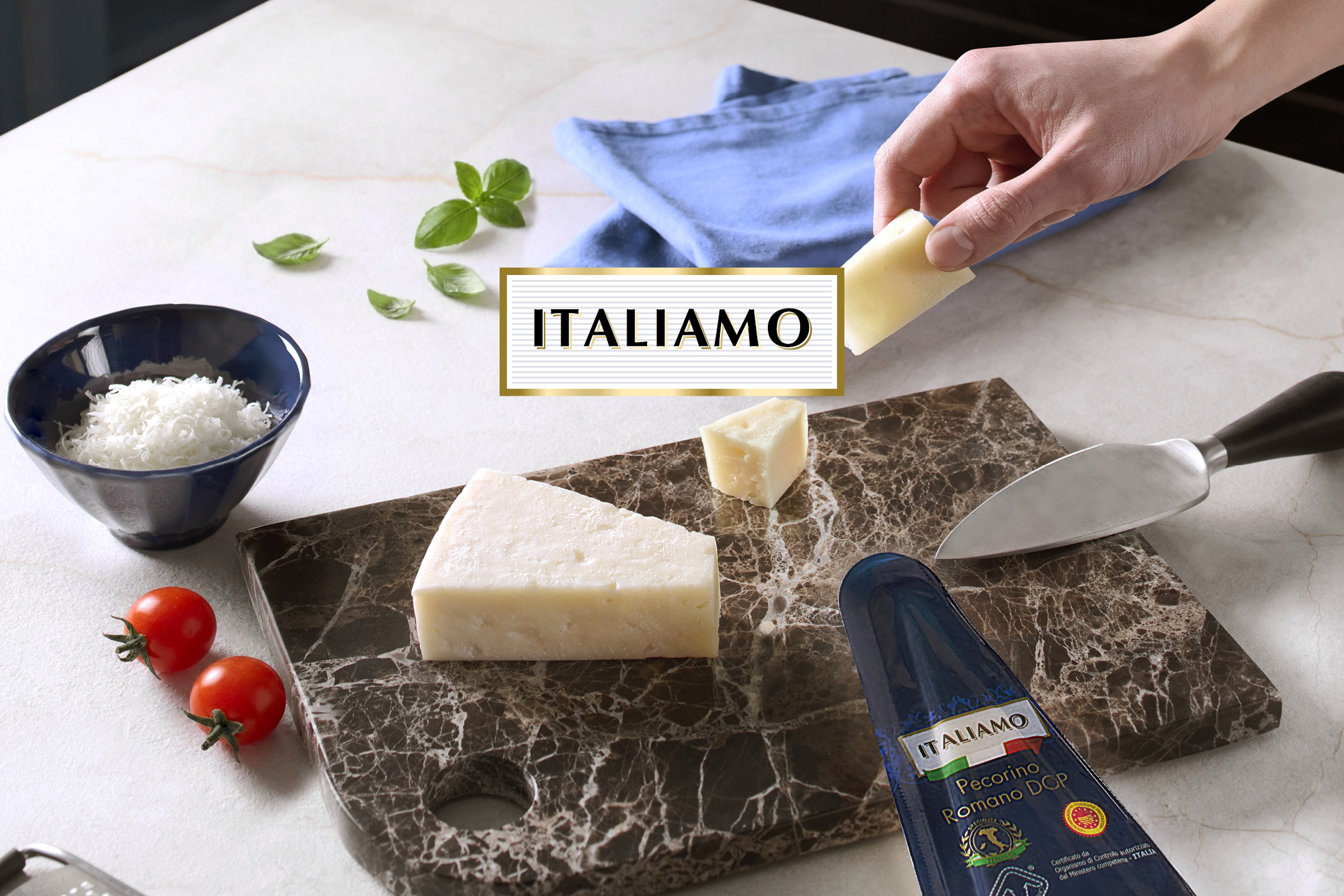Grated and block cheese on a marble board with cherry tomatoes, a knife, and 'ITALIAMO' text.