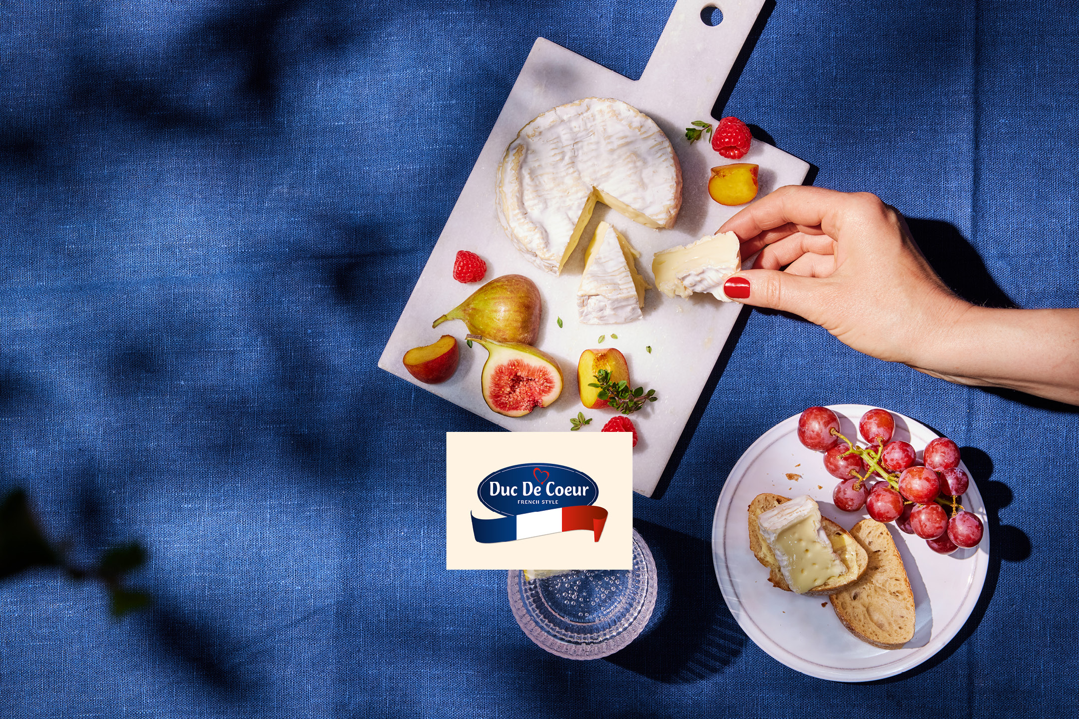 French-style cheese board with figs, raspberries, peaches, and grapes on a blue linen cloth.
