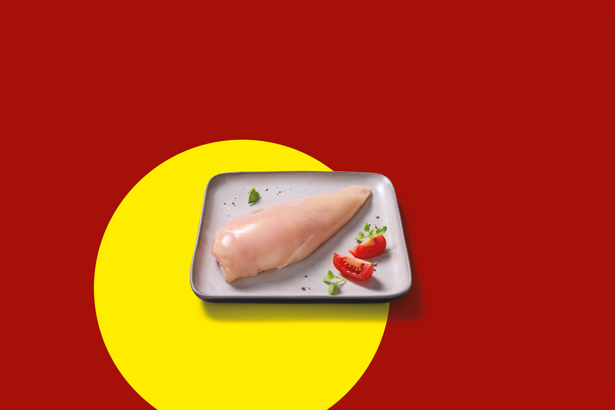 Raw chicken breast on a plate with tomatoes and herbs, on a red and yellow background.