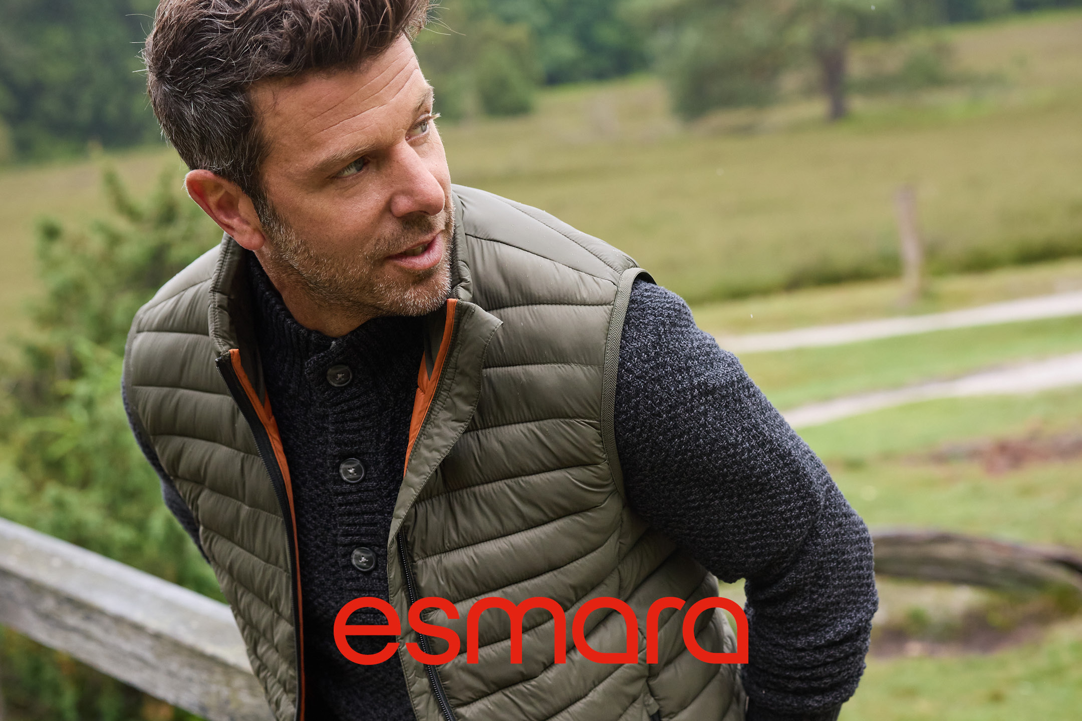 Man in a green quilted vest and dark knitted sweater outdoors.
