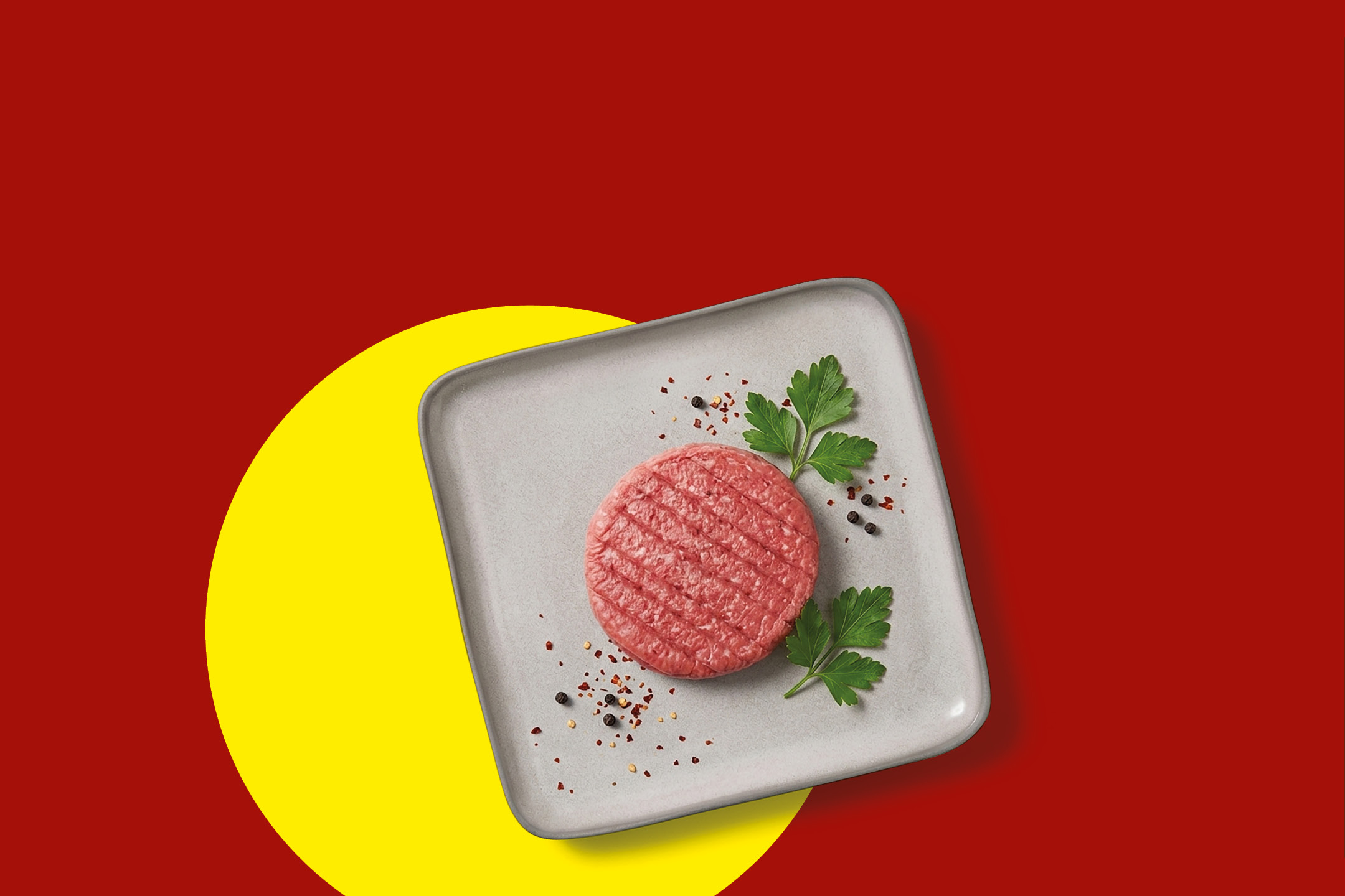 Raw burger patty with parsley and spices on a gray plate, red and yellow background.