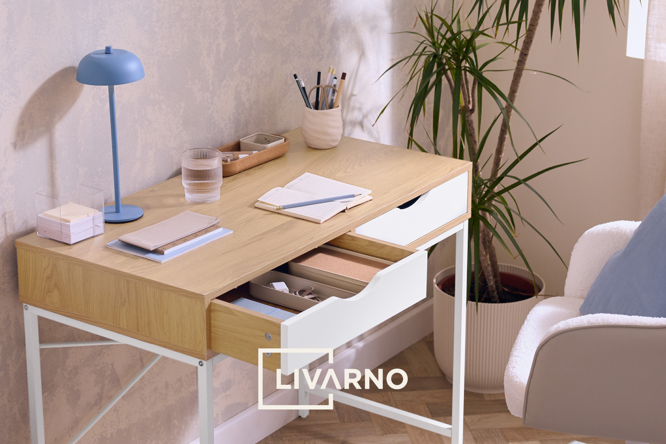 Wooden desk with office supplies, a glass of water, and a plant, in a light-toned room.