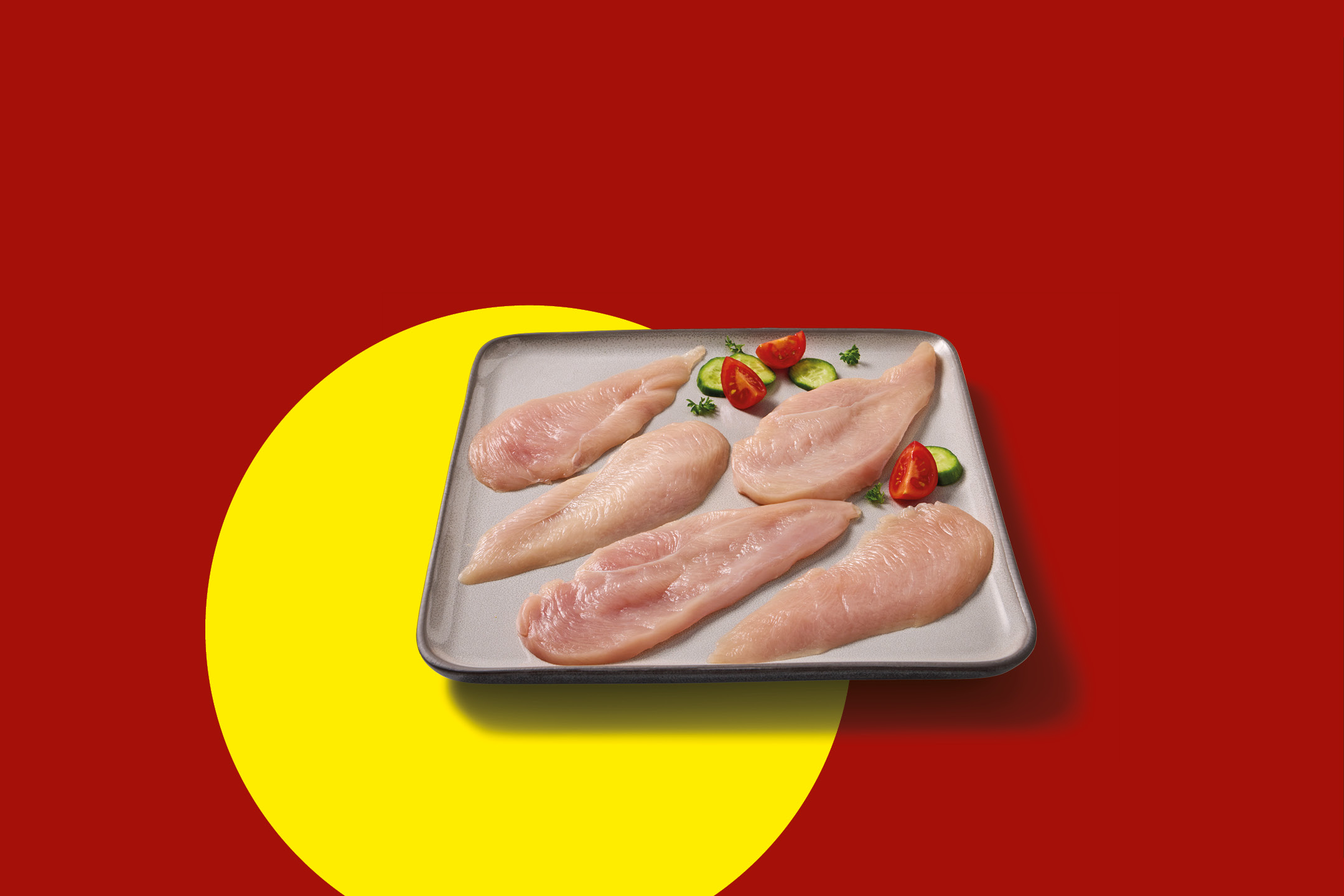 Raw chicken fillets on a grey plate with tomato and cucumber slices on a red and yellow background.