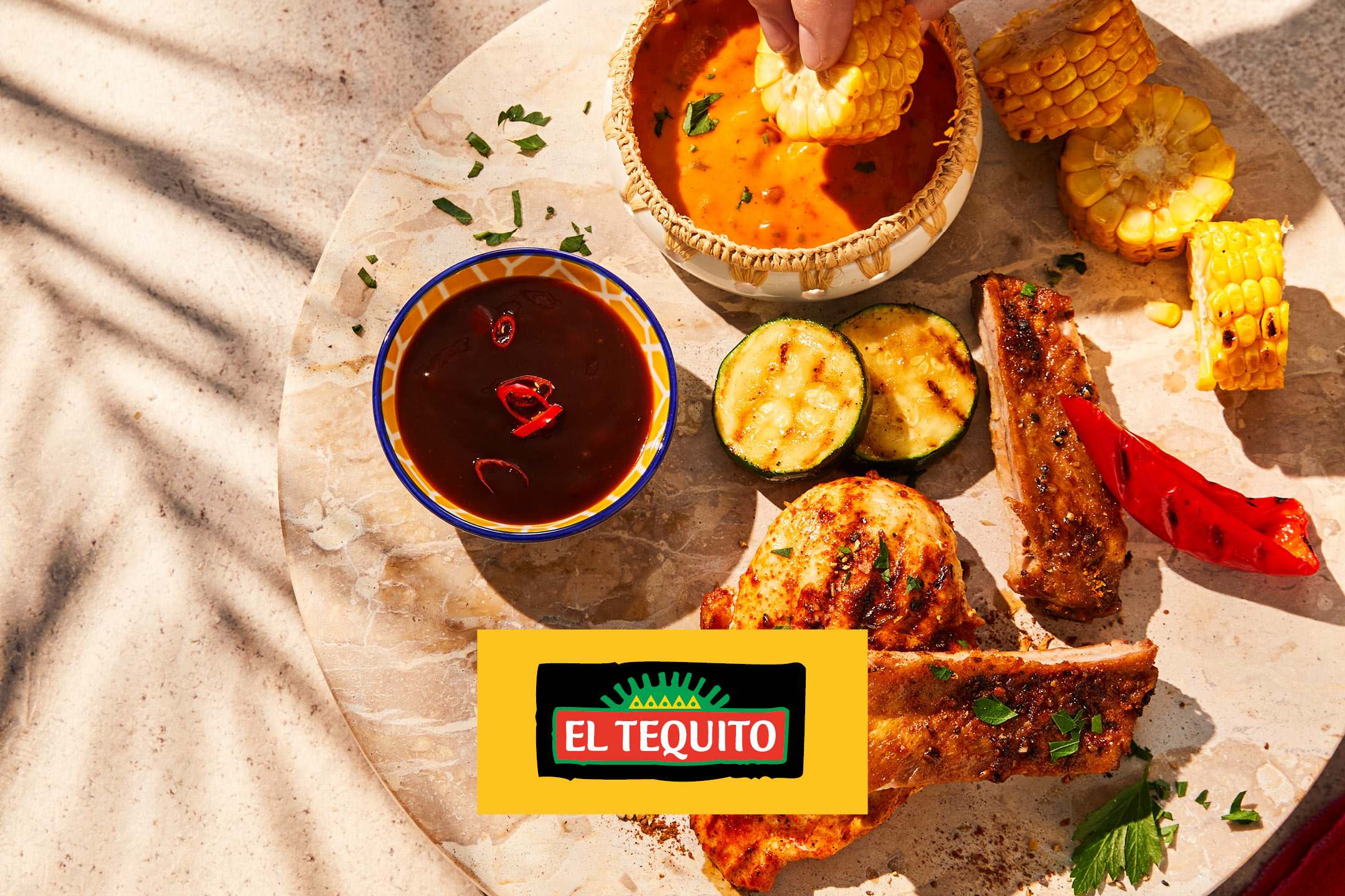 Grilled meats, vegetables, and sauces served on a stone platter under palm tree shadows.