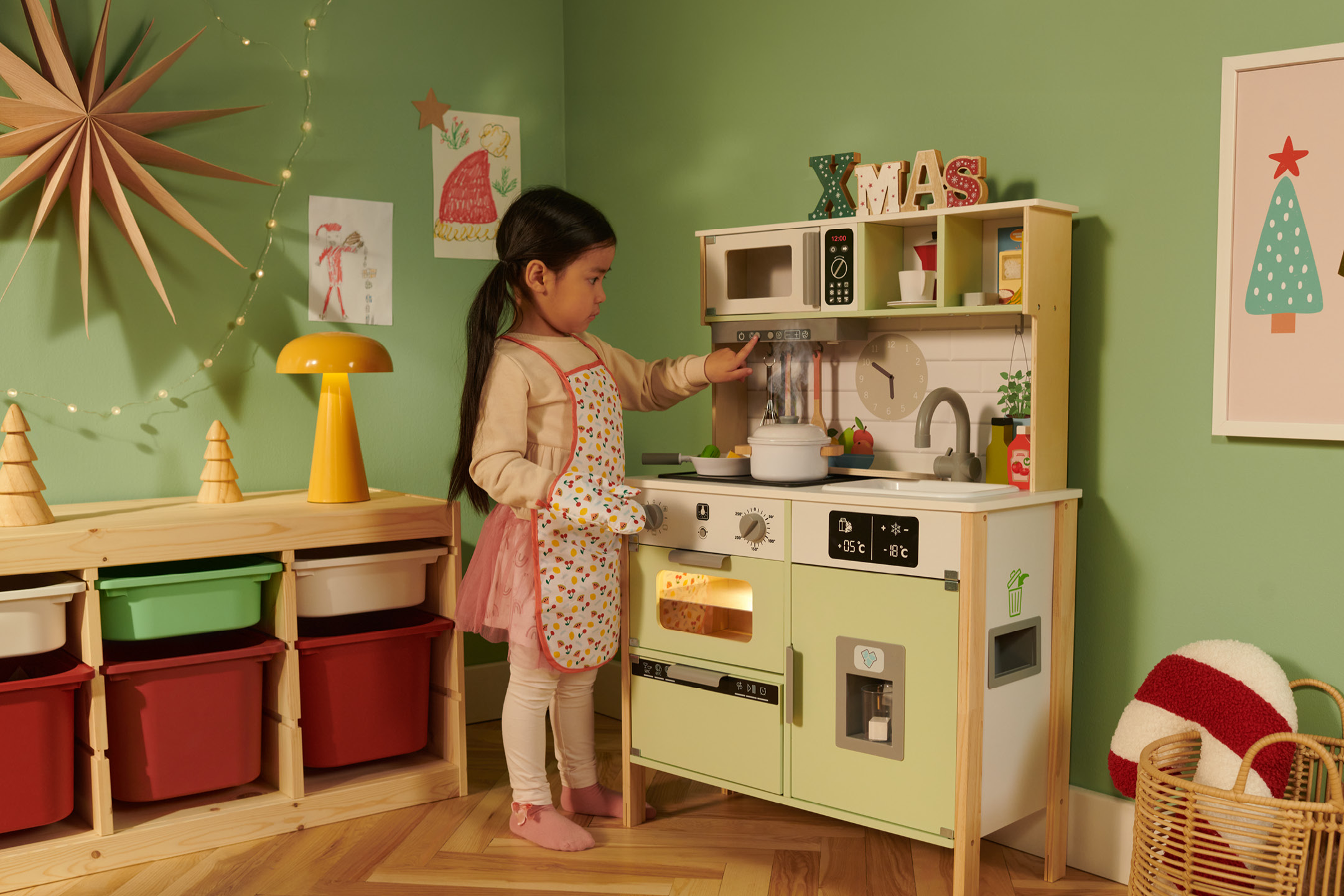 A young girl playing with a wooden toy kitchen decorated for Christmas.