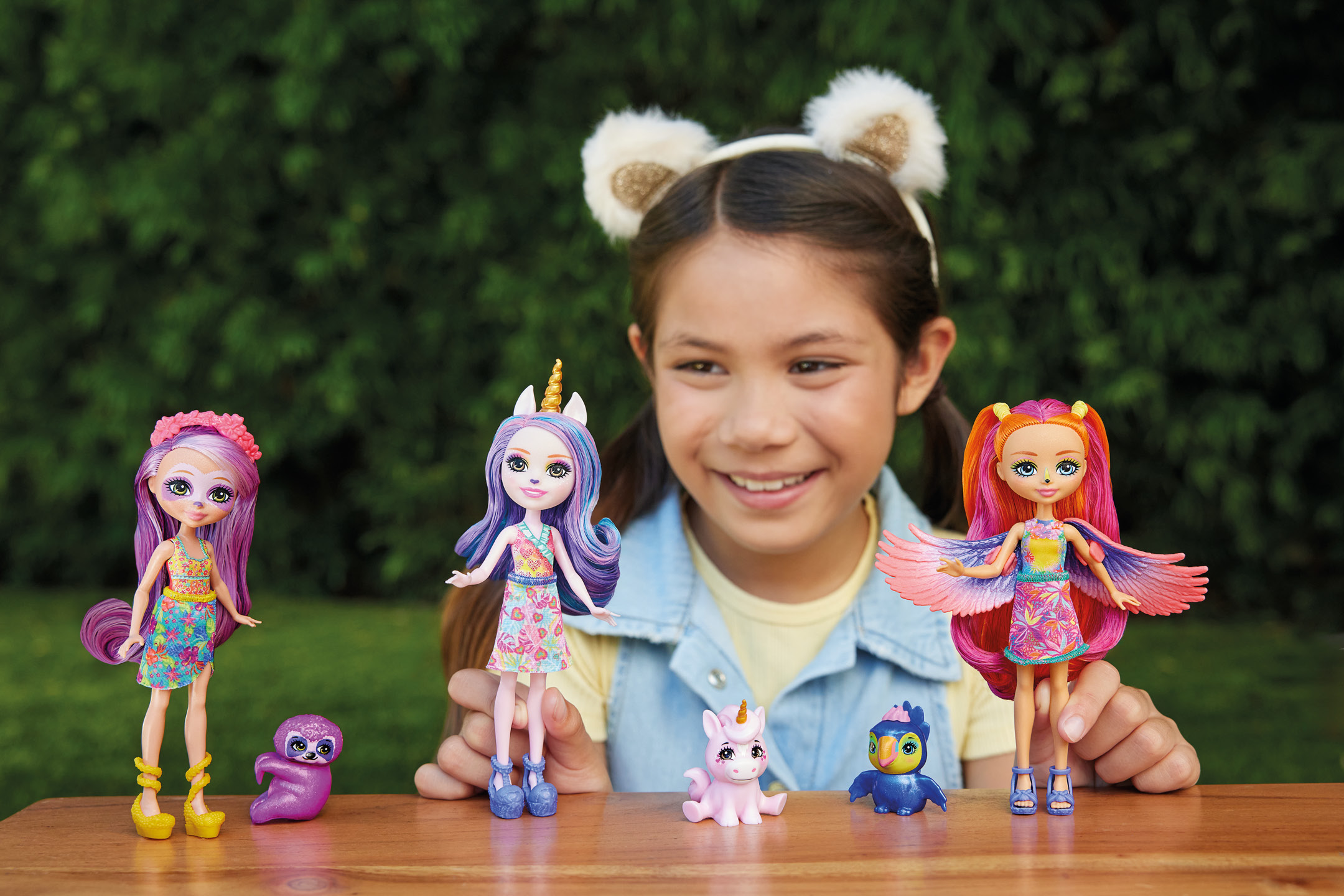 A smiling girl playing with three colorful fantasy doll figures outdoors.