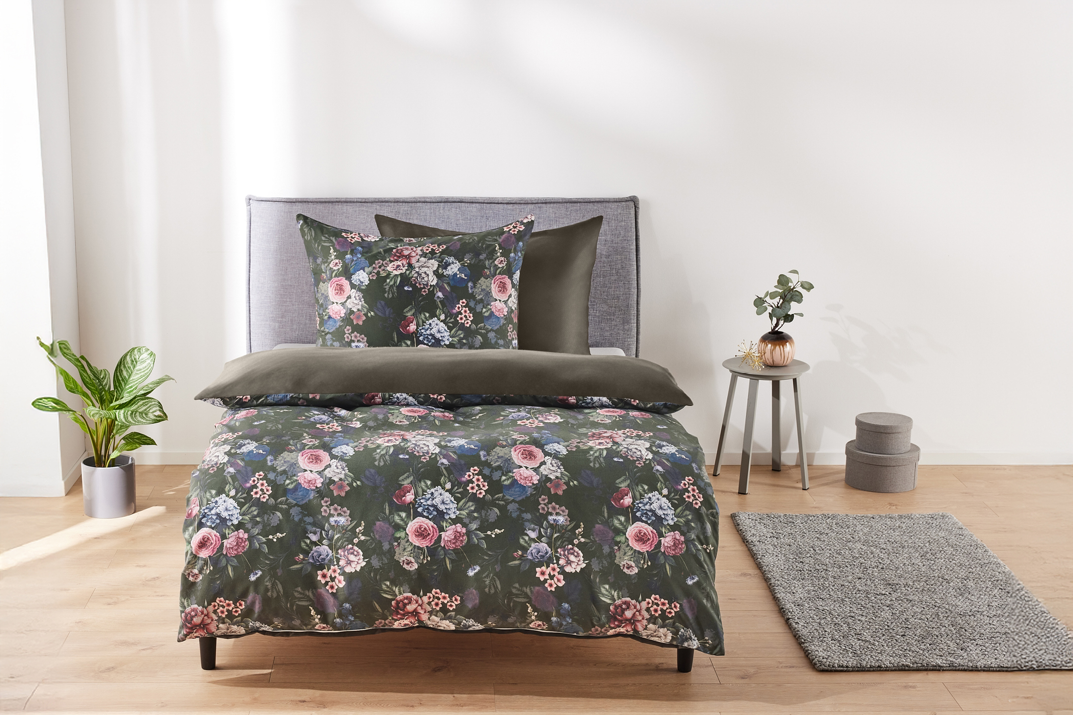 Bedroom with floral duvet cover set, grey headboard, and side table with plant.