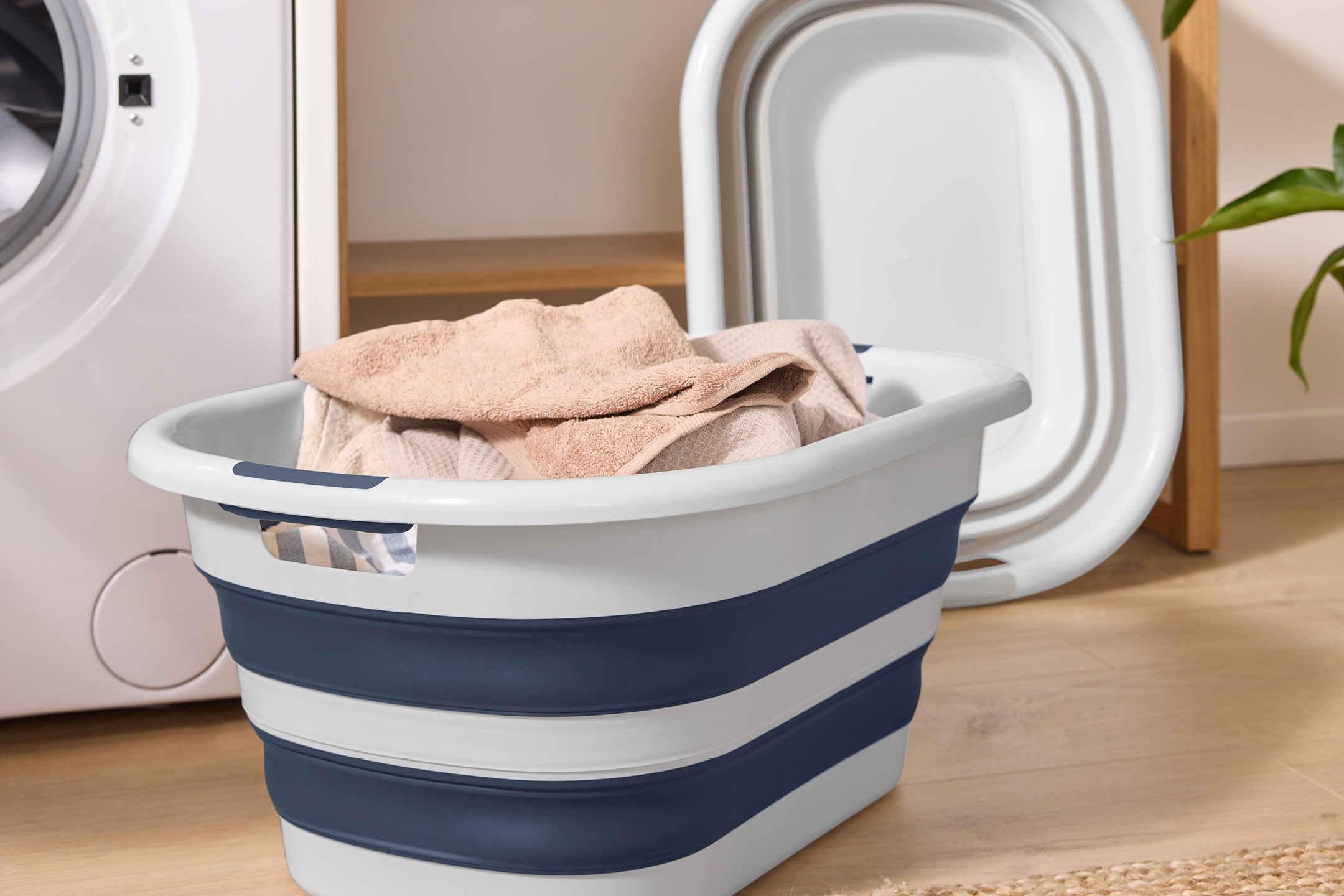 Collapsible laundry basket with towels next to a washing machine and a foldable tub.