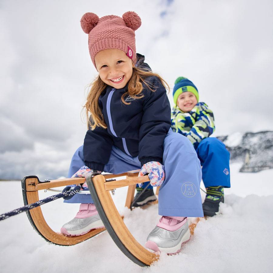 Children in winter clothes and bobble hats, sledding in the snow.