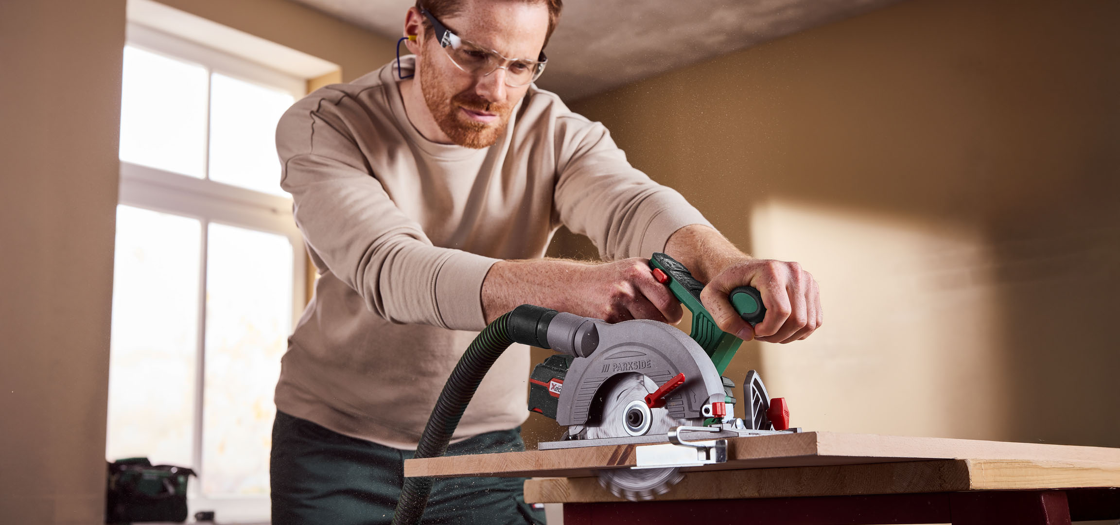 Man using a Parkside circular saw to cut wood, wearing safety glasses and ear protection.