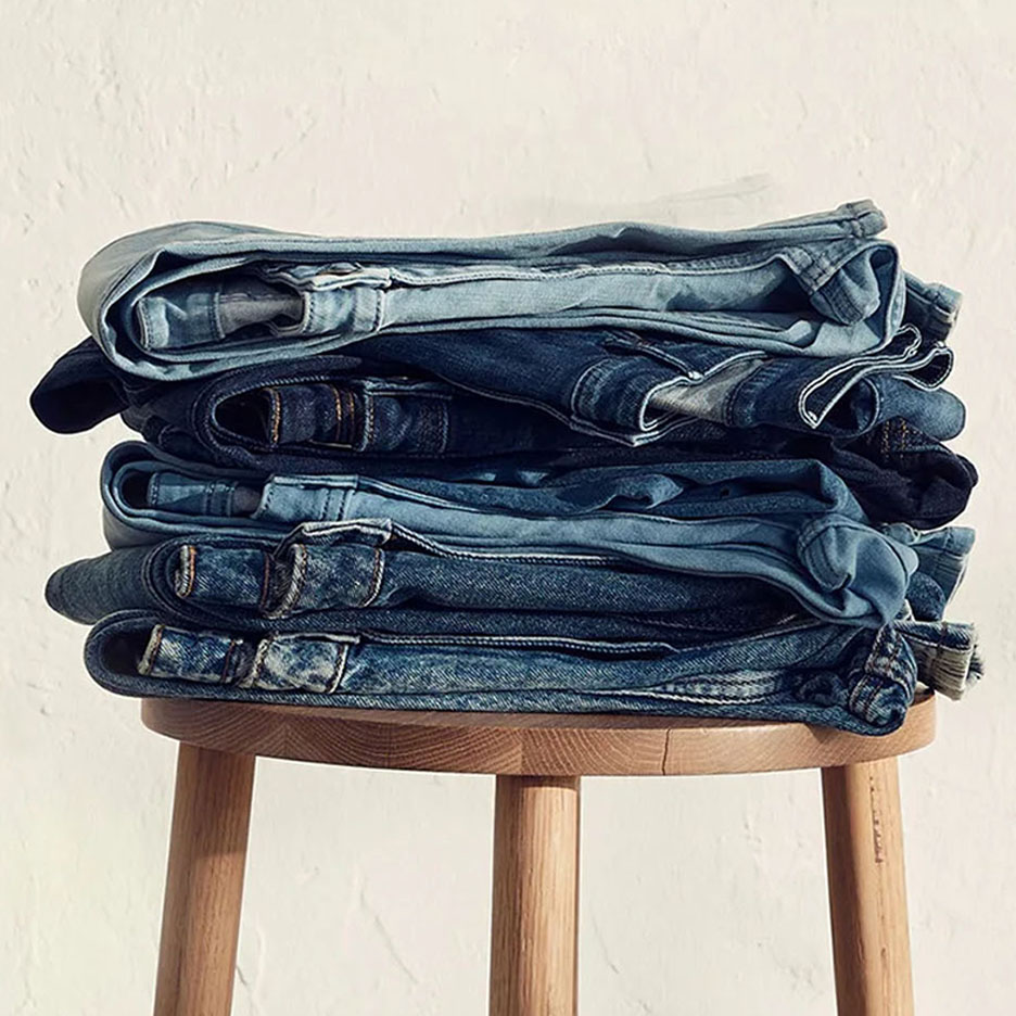 A stack of jeans in various shades of blue on a wooden stool.