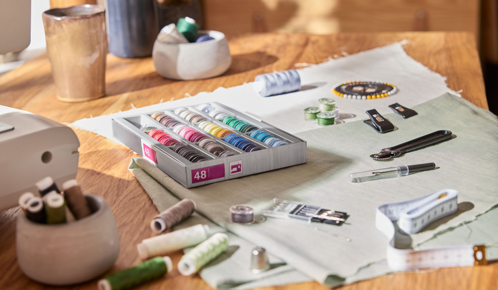 Sewing kit with a box of colorful threads, sewing machine, and various tools on a wooden table.
