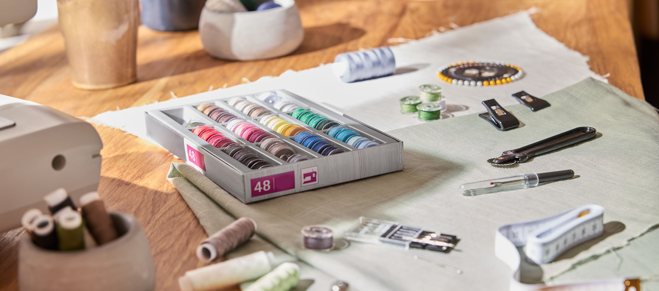 Sewing supplies on a wooden table, including a thread organizer with 48 spools, fabric, and various tools.