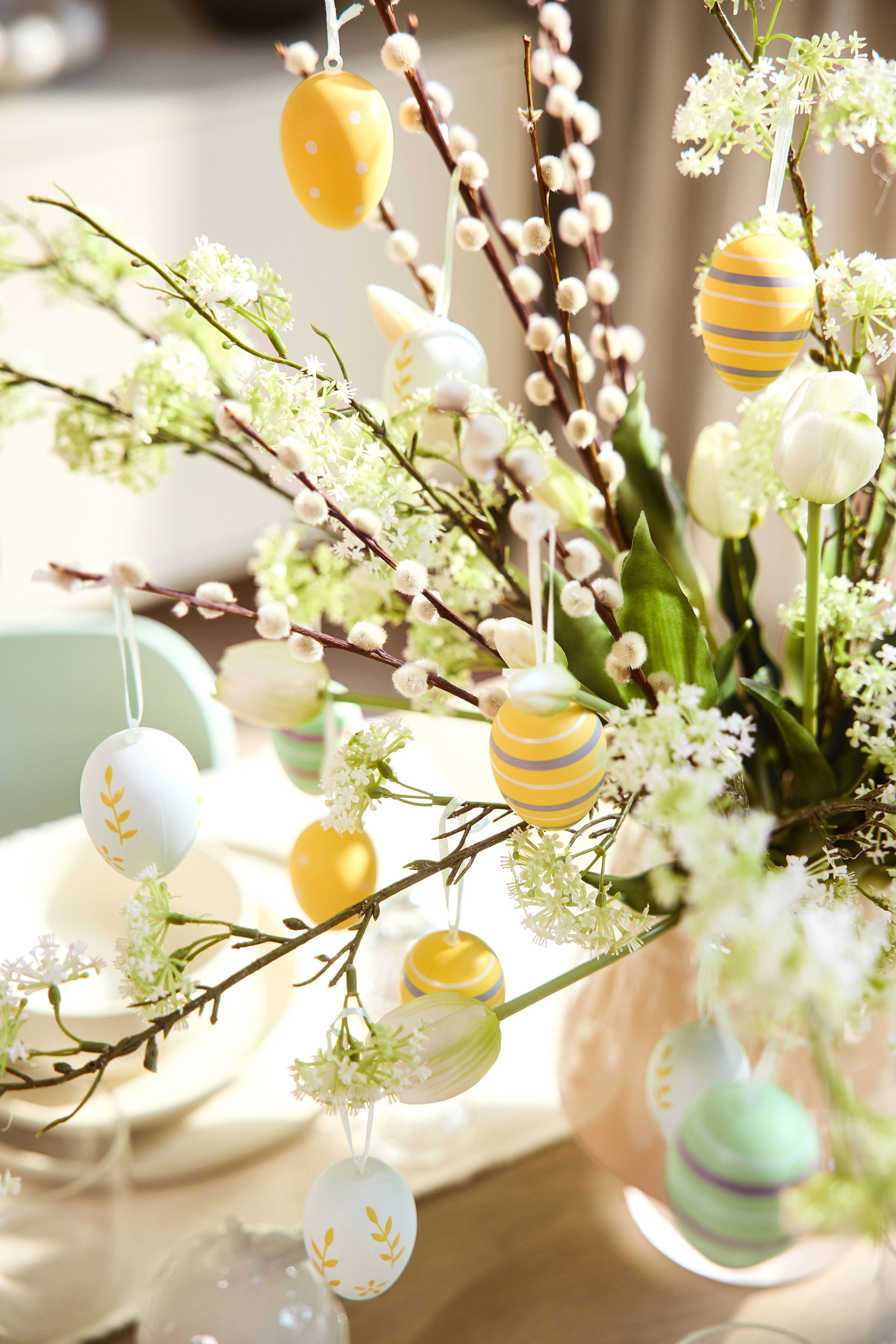 Easter decoration with pussy willow branches, white flowers, and colorful eggs.
