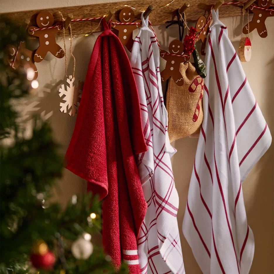 Red and white Christmas kitchen towels hanging on a wooden wall rack with gingerbread decorations.