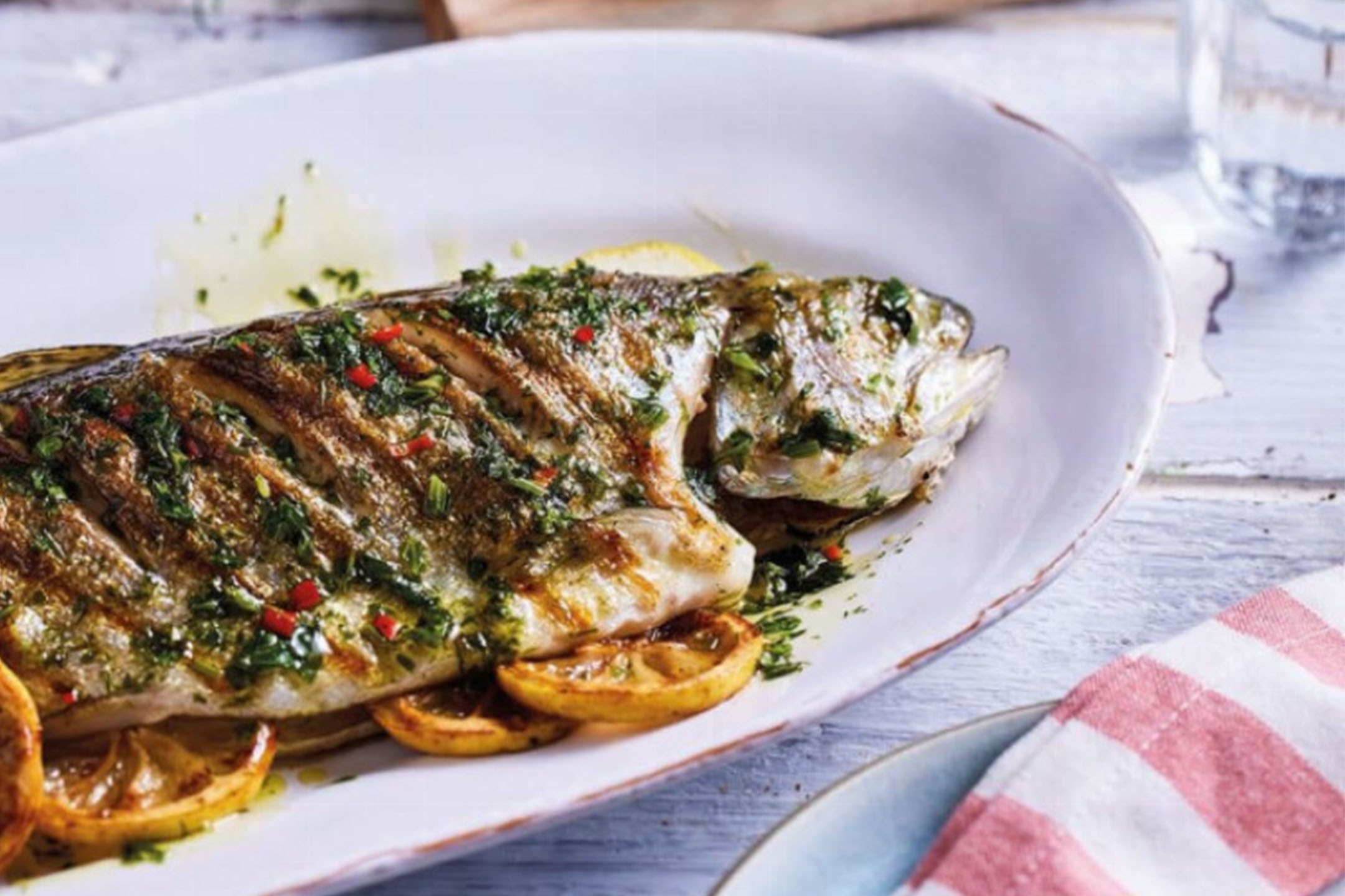 Grilled whole fish with herbs and lemon on a white platter.