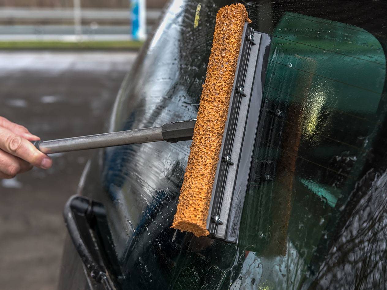 Window cleaner with long handle cleaning a car's rear window.