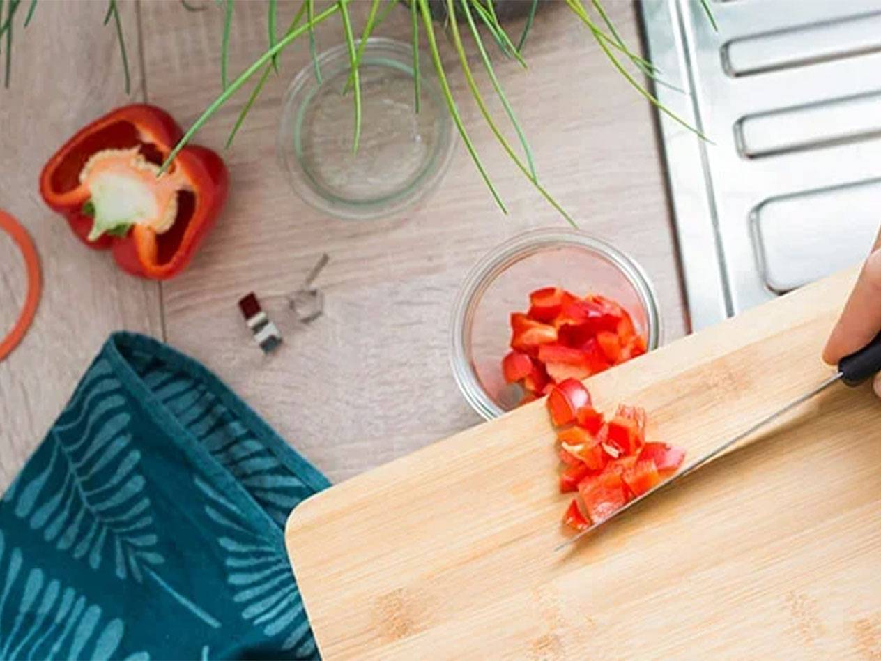 Cut red bell pepper on a wooden cutting board, with a towel and sink in the background