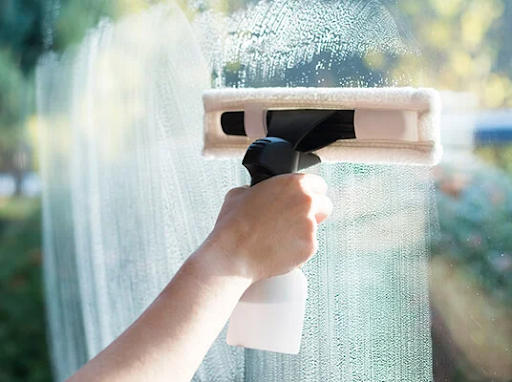 Hand cleaning a window with a window washer and spray bottle.