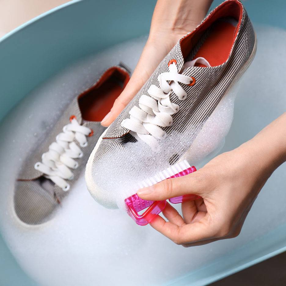 Hands scrubbing sneakers with a brush in soapy water.