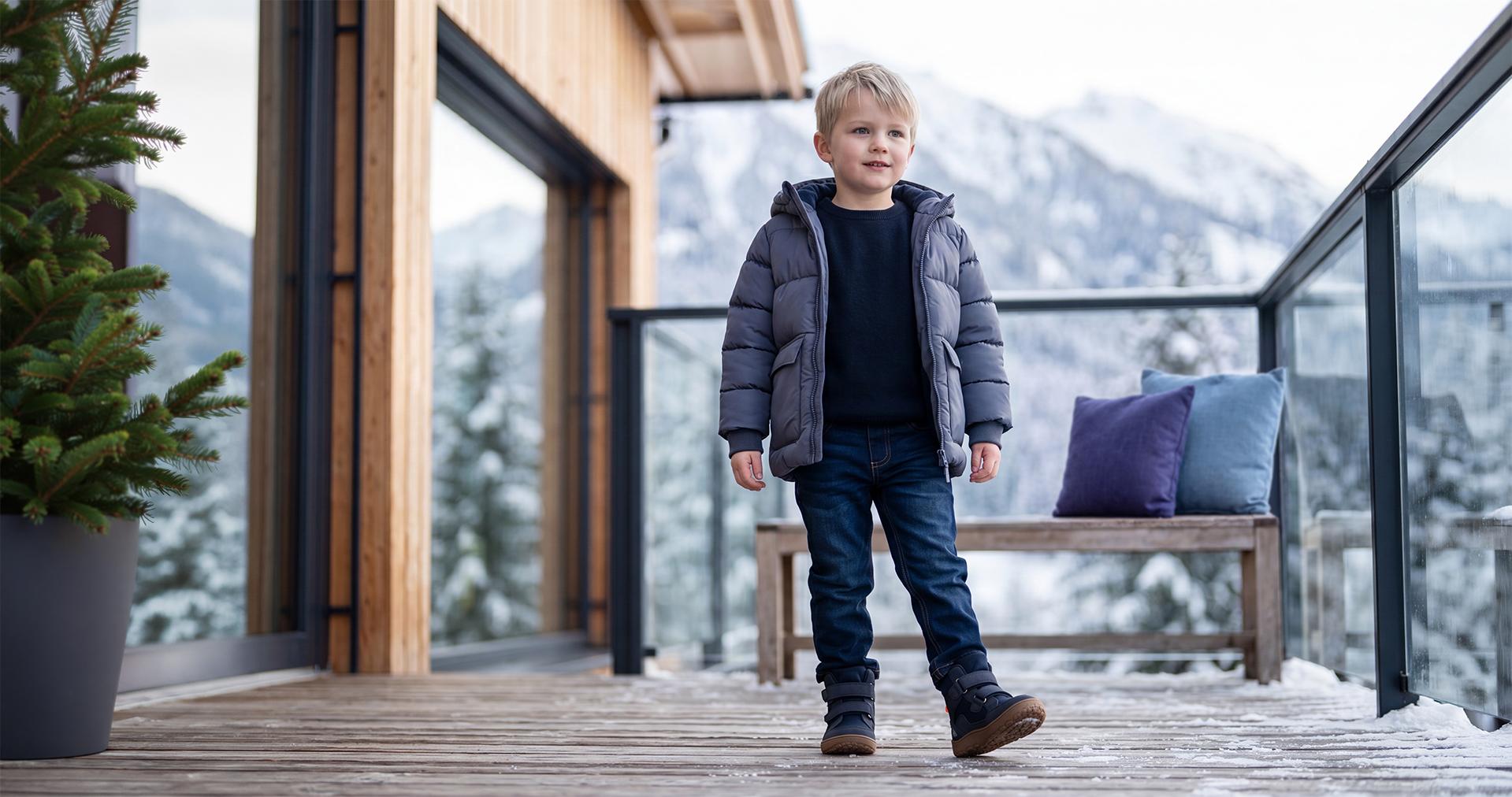 Young boy in a warm winter jacket, jeans, and boots on a mountain terrace