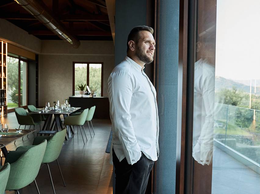 Man in white shirt looking out window in a restaurant with green chairs.