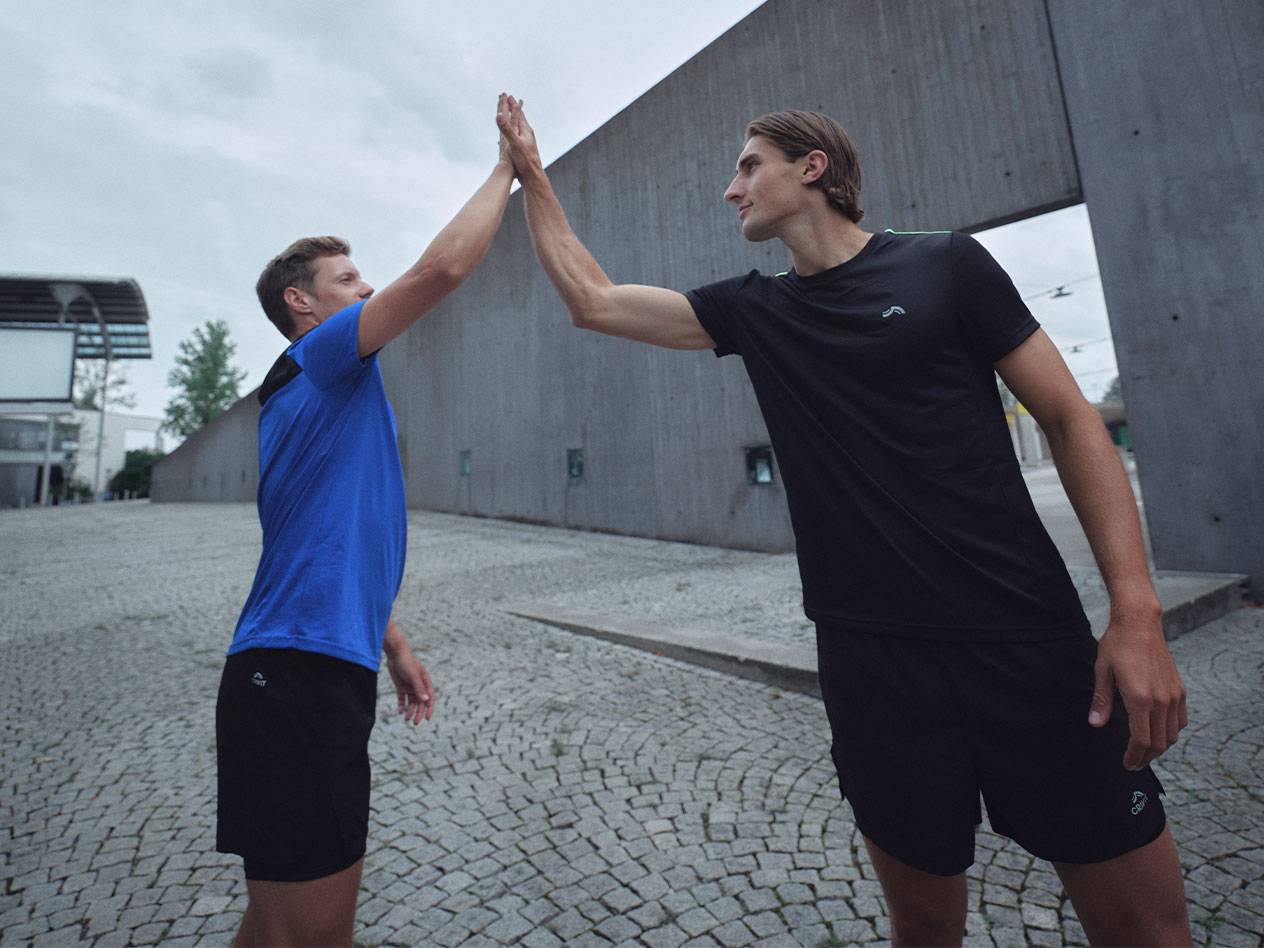 Two men in black and blue sports t-shirts and shorts giving a high-five.