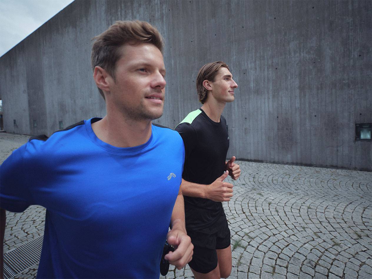 Two men running in sports t-shirts and shorts, one blue and one black.
