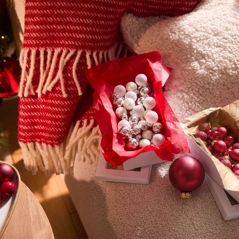 Christmas decorations: red and silver baubles in boxes, with a blanket and cushion.