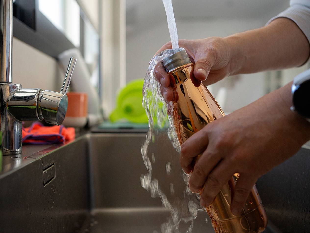 Person filling a copper water bottle from a tap in a kitchen sink.