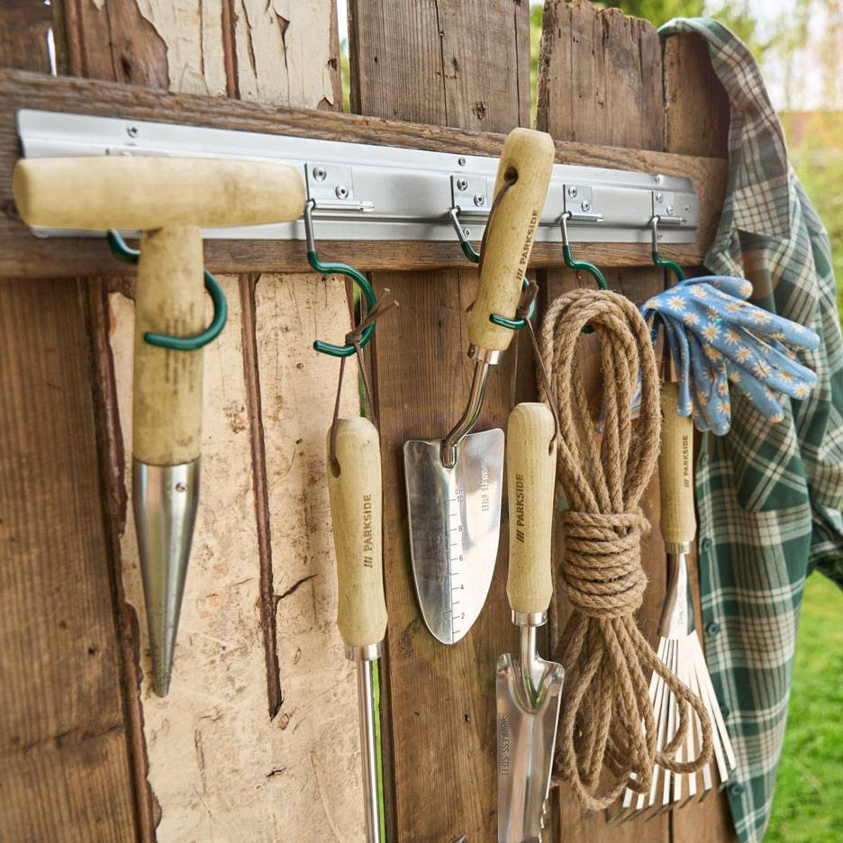 Garden tools and rope hanging on a wooden wall, next to a shirt and gloves.