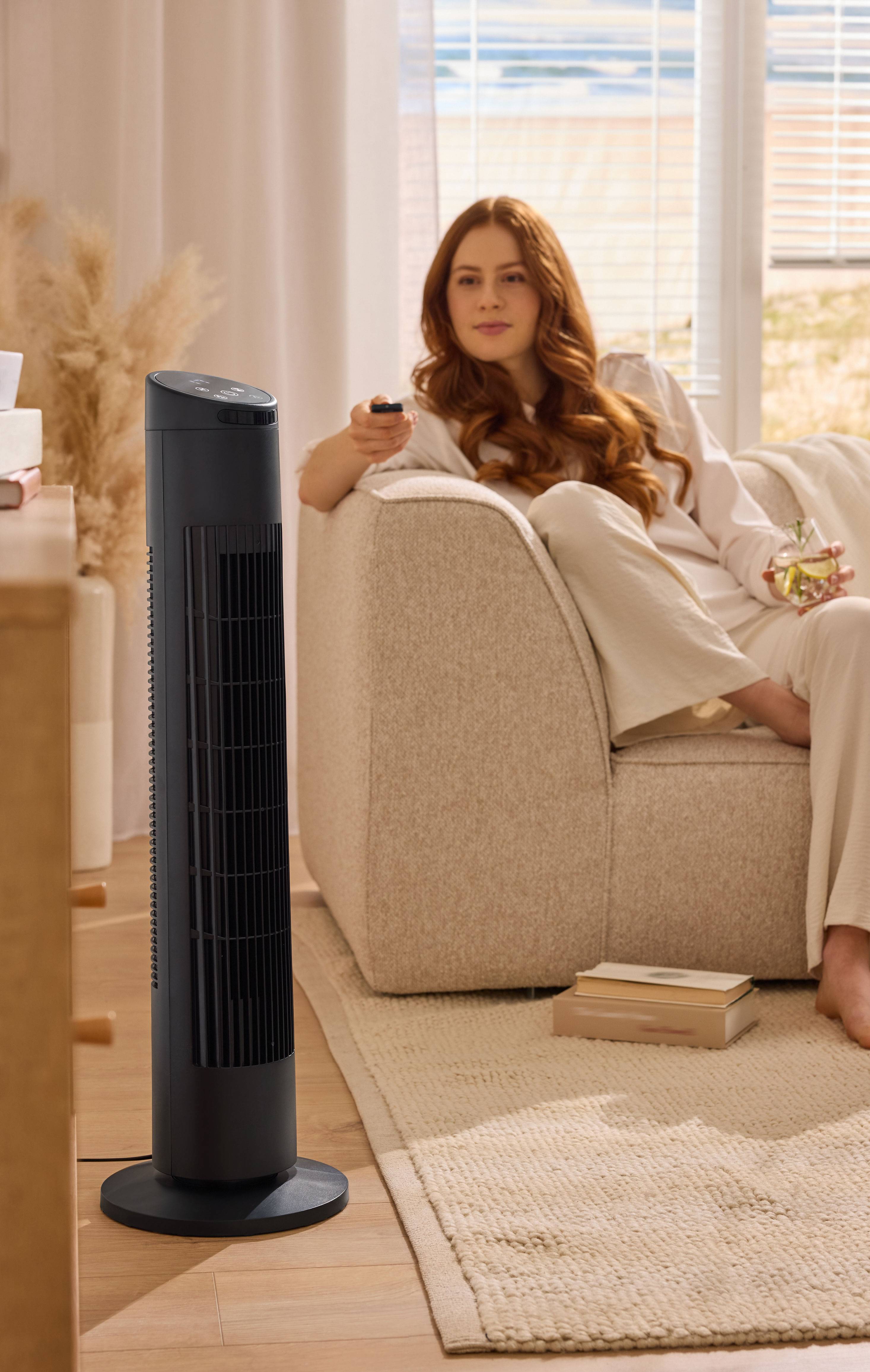 Woman relaxing on a sofa with a tower fan in a living room.