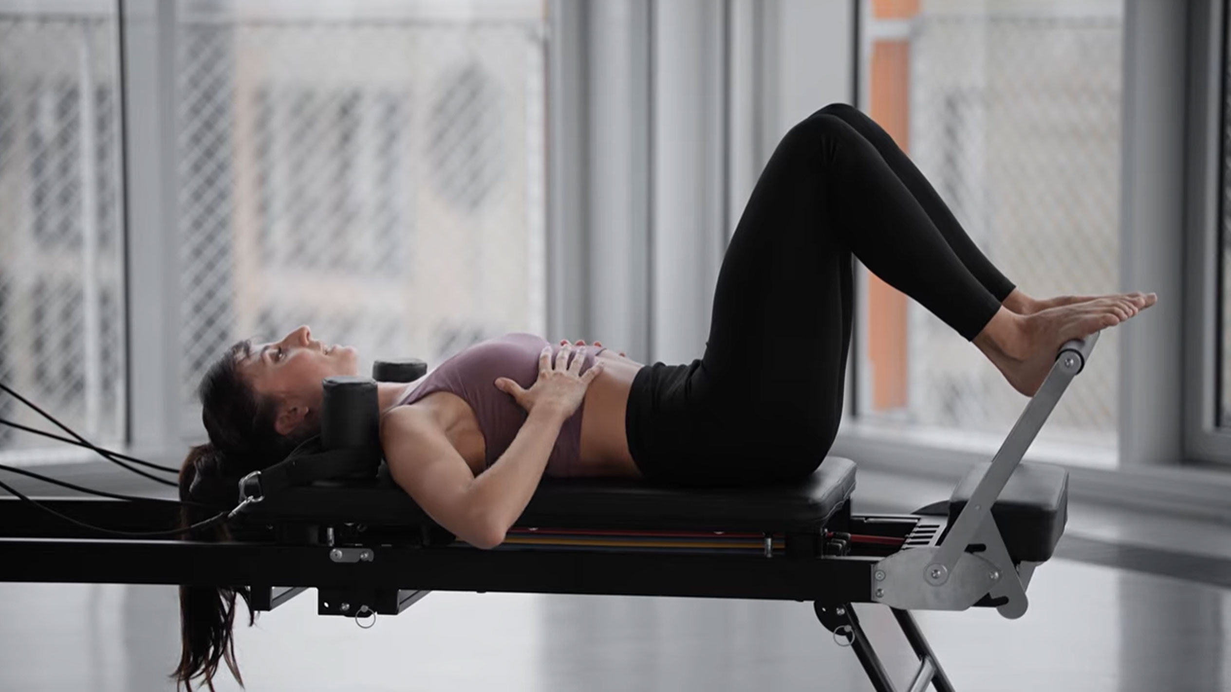 Woman doing Pilates on a reformer, with hands on her chest.