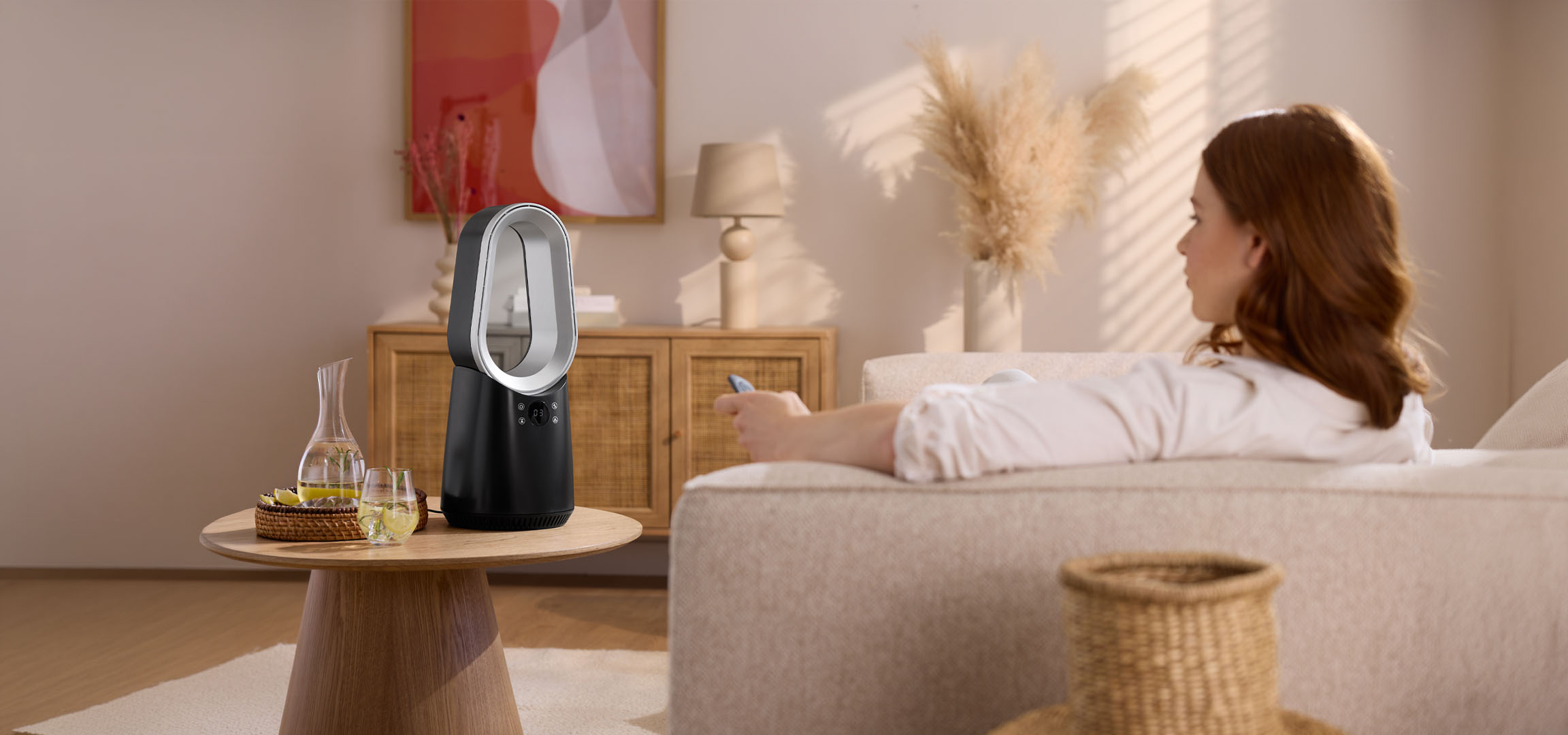 Woman on sofa with remote, modern fan and drinks on table.