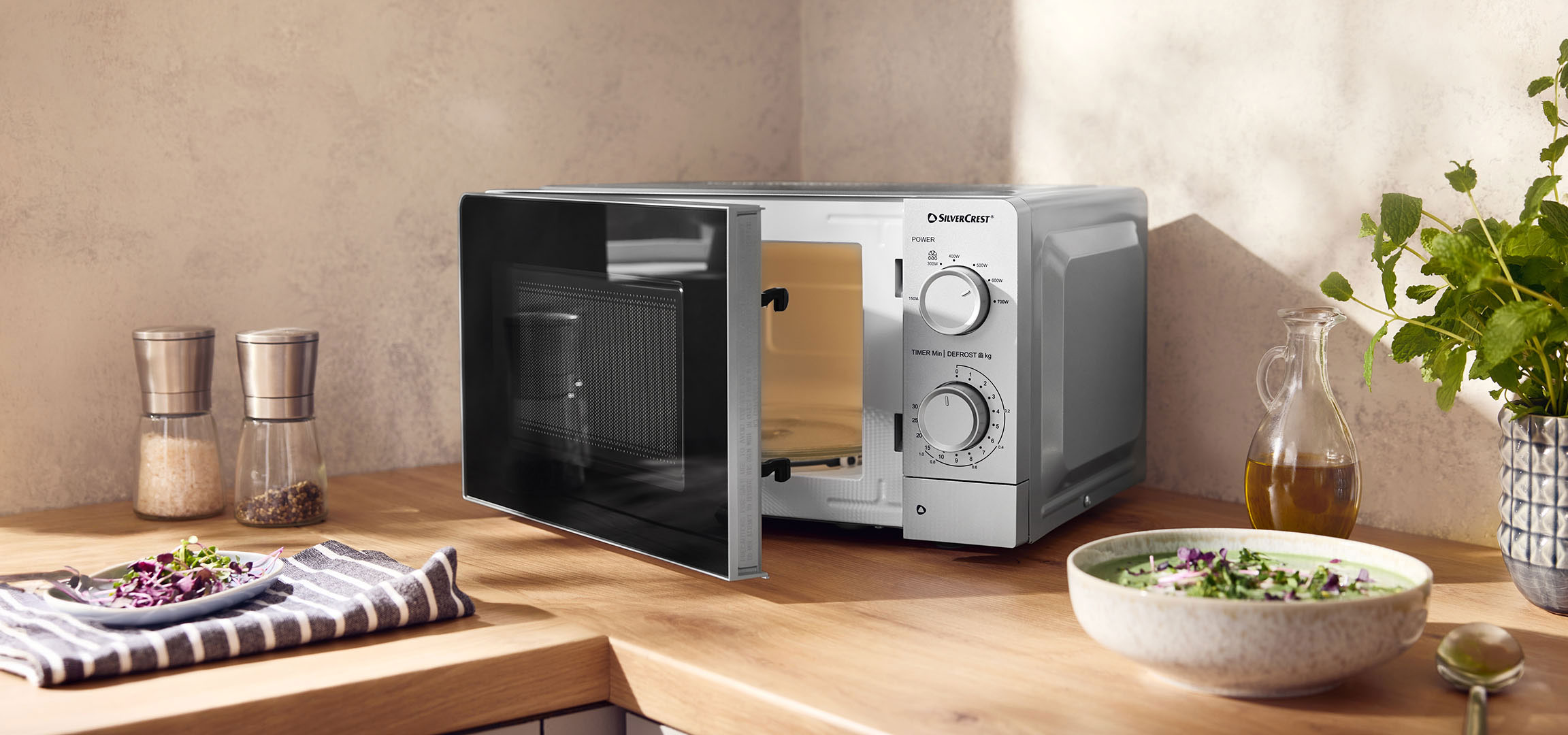 aiLabeling.aiLabelForImageAltText: Microwave oven with an open door on a wooden counter, with spices and bowls.