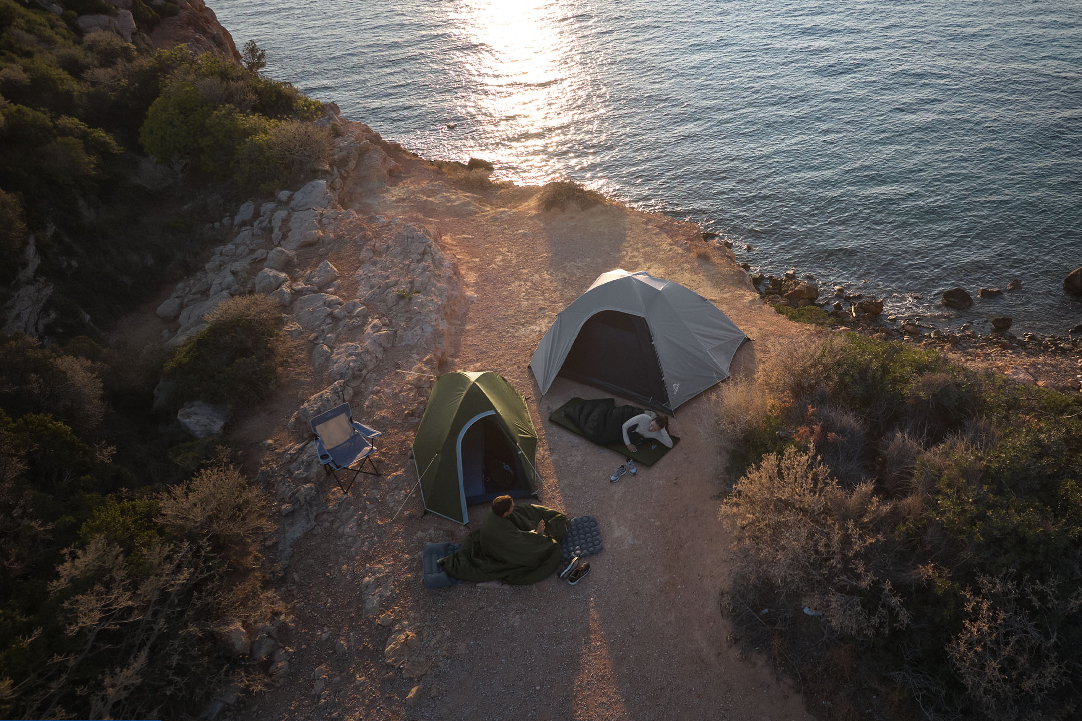 Two tents and sleeping bags on the coast at sunset.