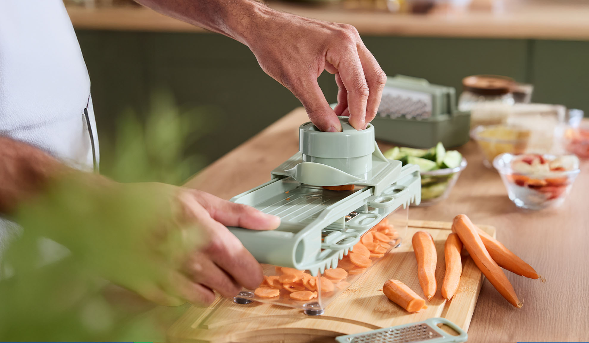 A man uses a mandoline to slice carrots on a wooden cutting board.