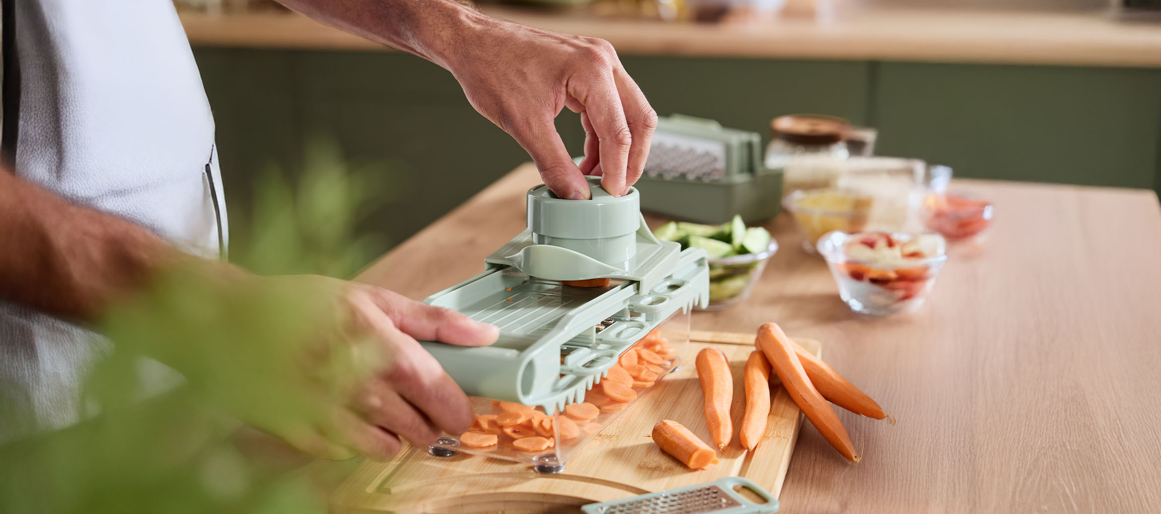 Person slicing carrots with a mandoline slicer on a wooden cutting board.