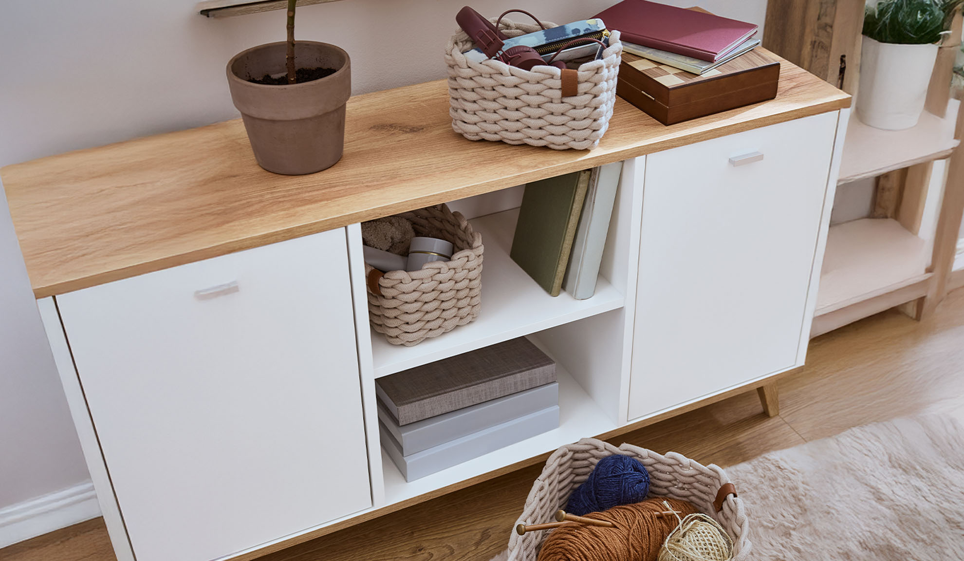 White sideboard with a wooden top, decorated with plants, baskets, and books.