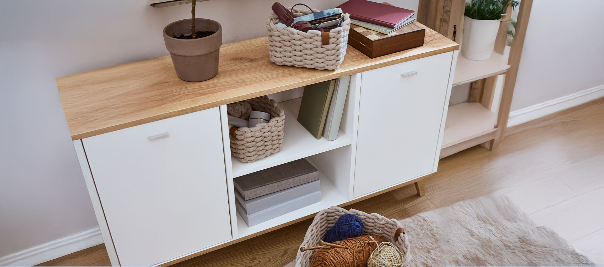 White and wood sideboard with storage baskets, books, and a plant.
