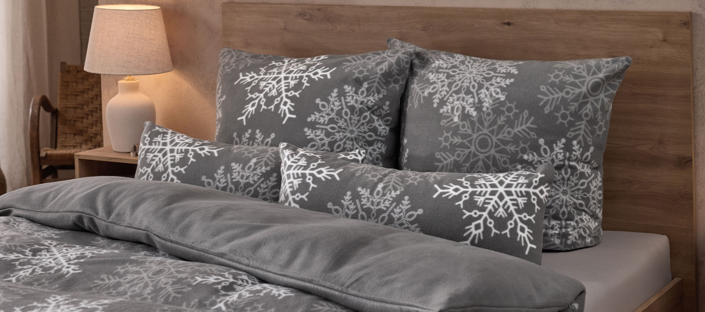 Grey bedding with snowflake pattern and matching pillows in a cozy bedroom.