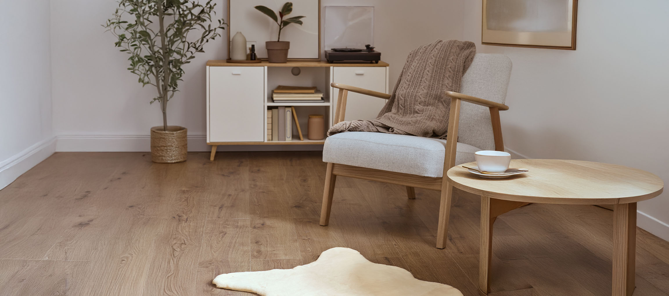 Grey fabric armchair with knitted throw, wooden coffee table, and modern sideboard.