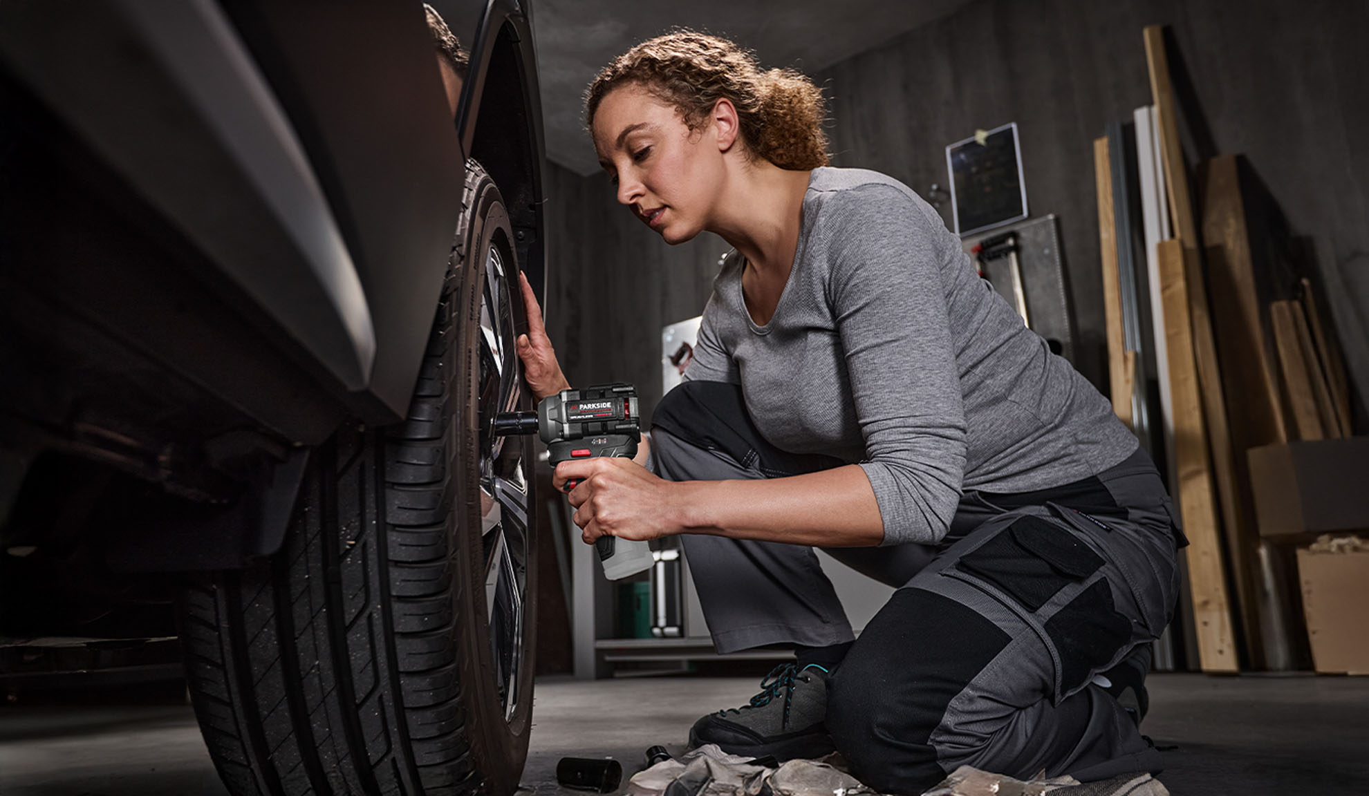 Woman using a Parkside impact wrench to change a car tire in a garage.