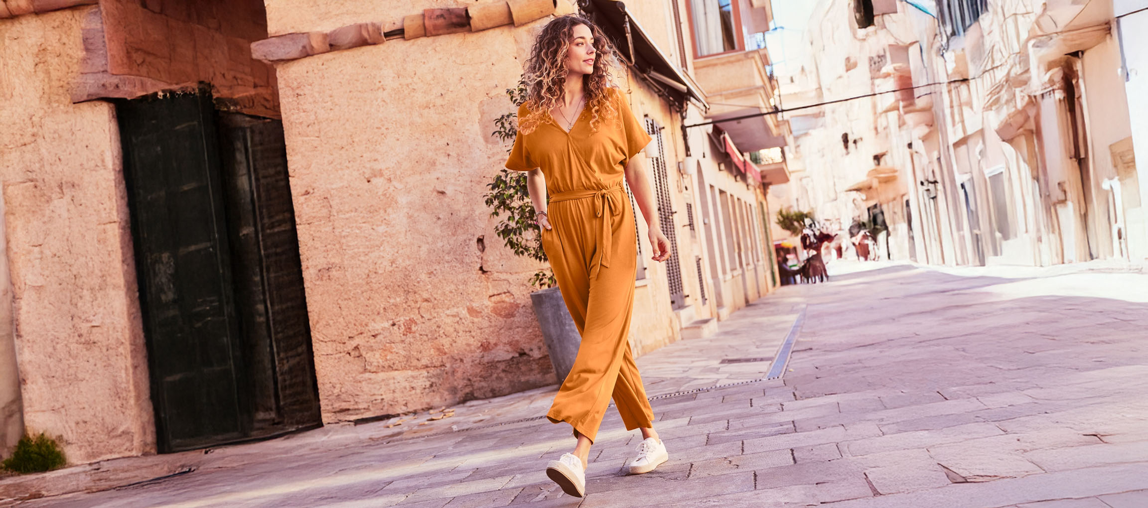 Woman walking down a street in a mustard yellow jumpsuit.