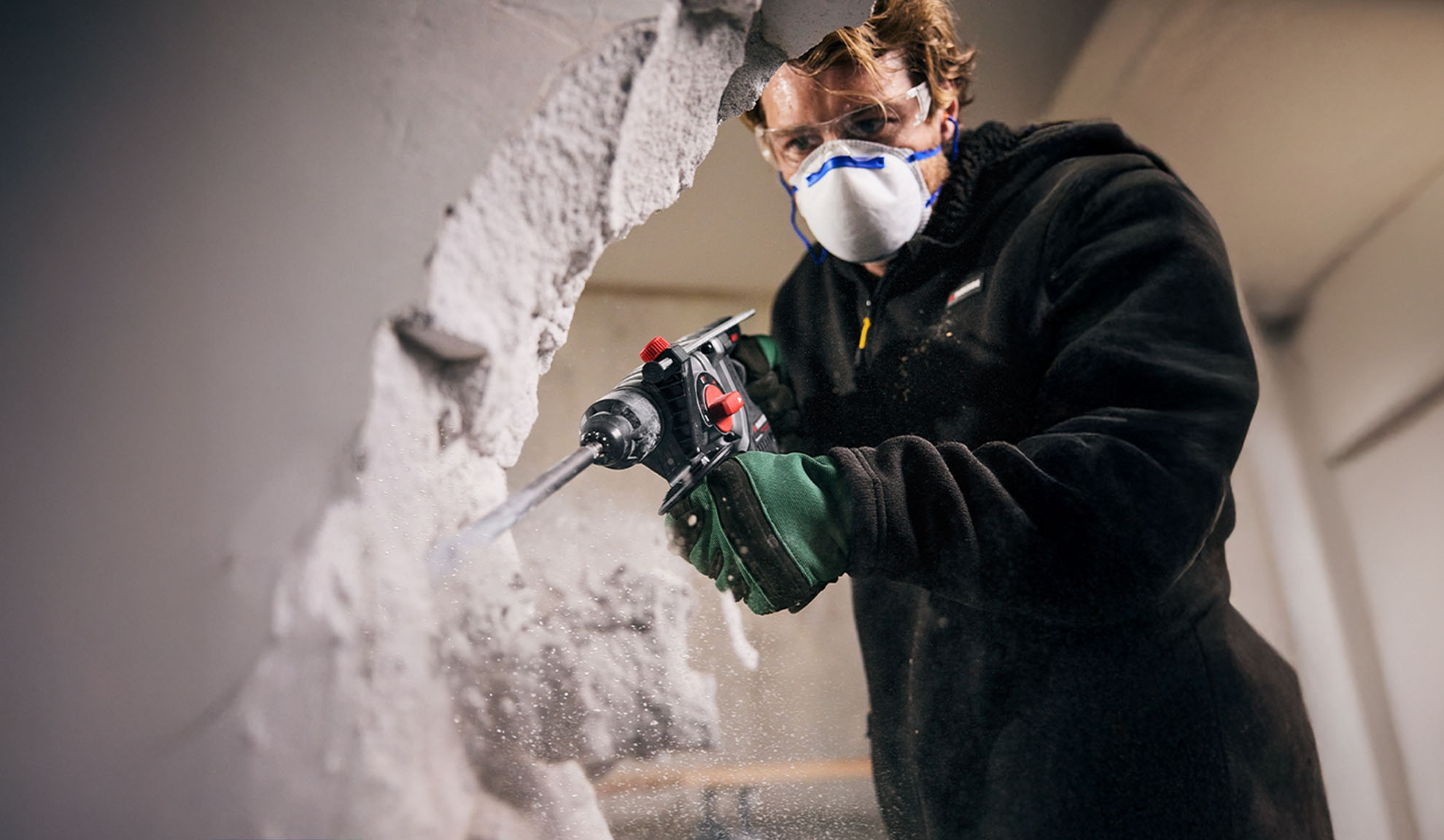Man in safety gear using a hammer drill to break through a wall