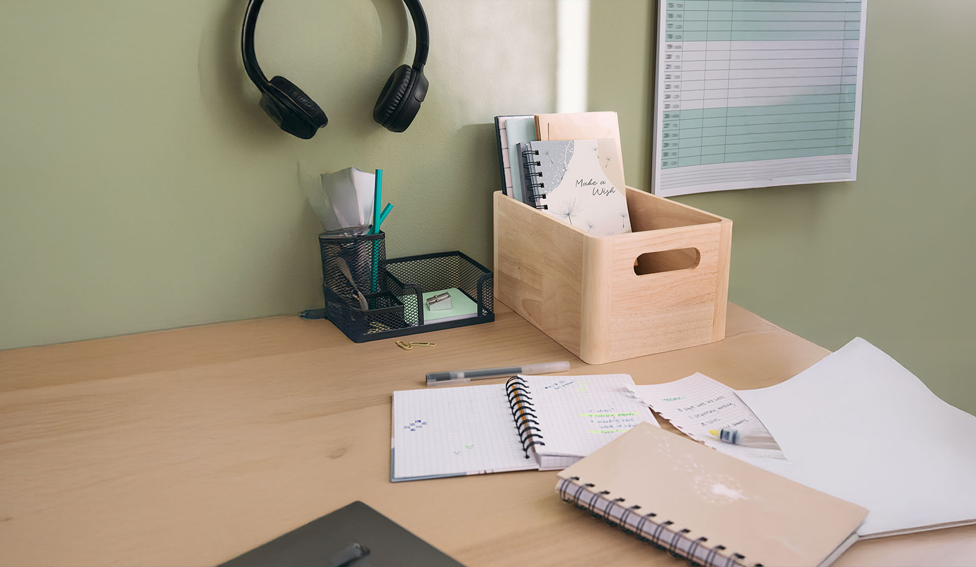 Desk with headphones, mesh organizer, wooden box with notebooks, and office supplies.