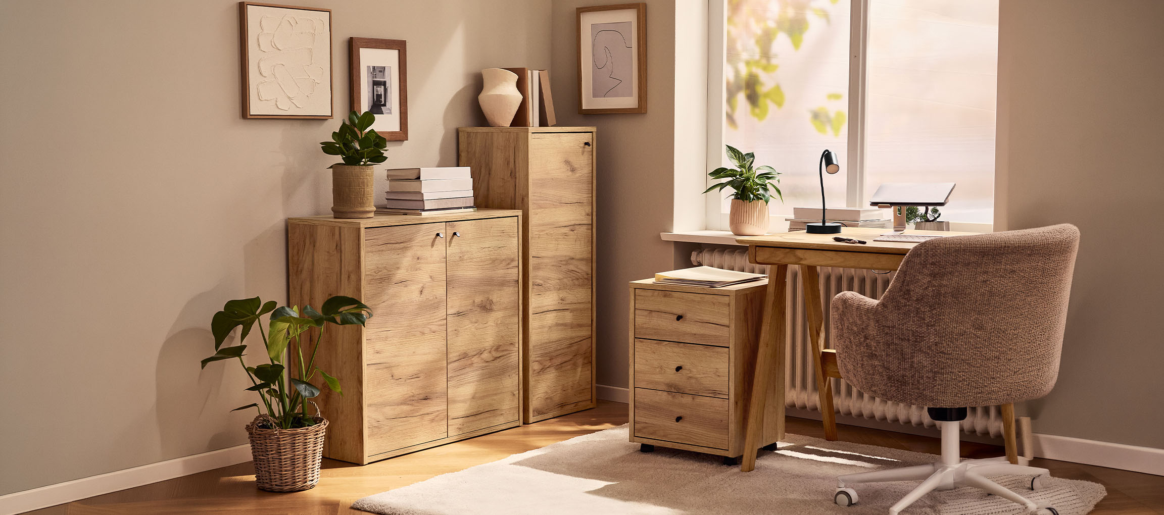 Home office with wooden cabinets, desk, and chair, decorated with plants and pictures.