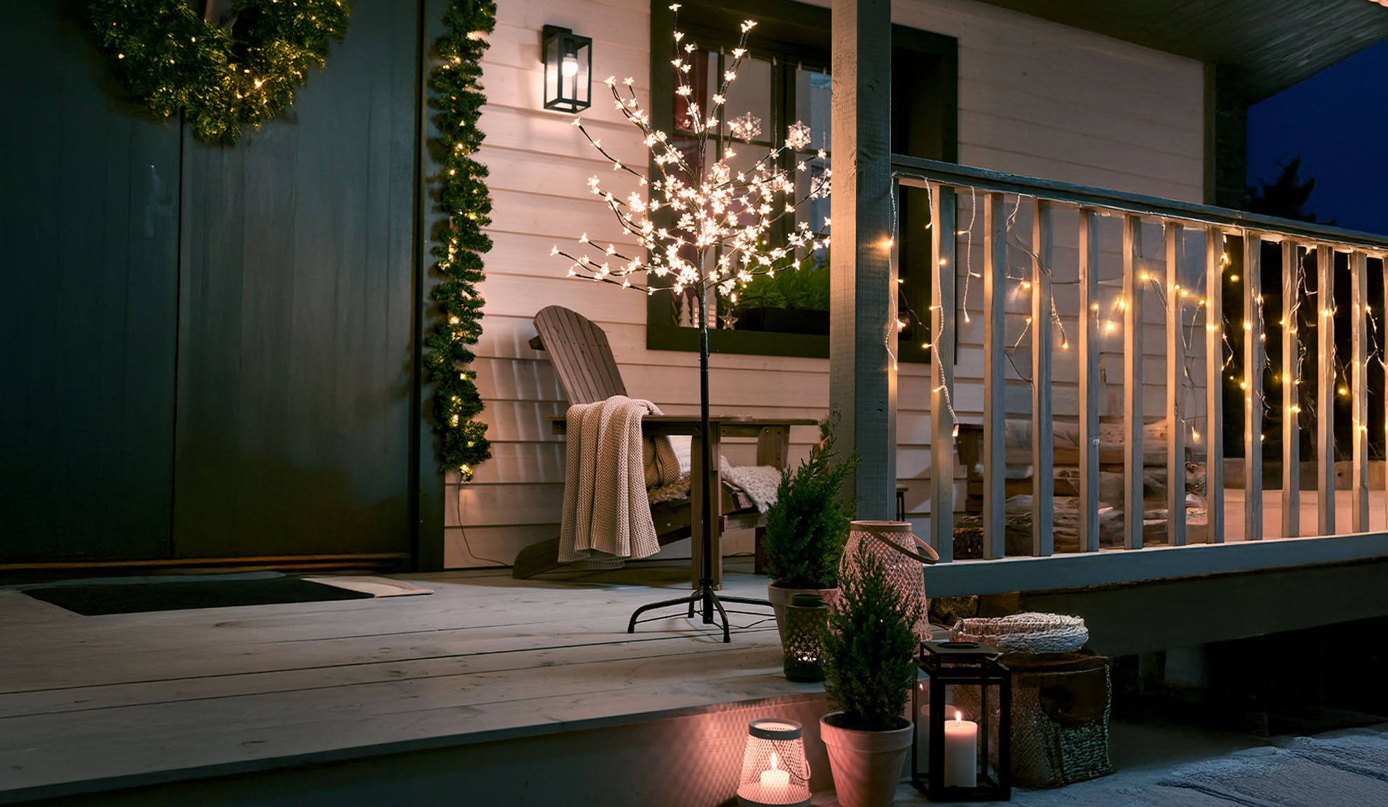 Porch decorated with Christmas lights, a wooden chair, and potted plants.